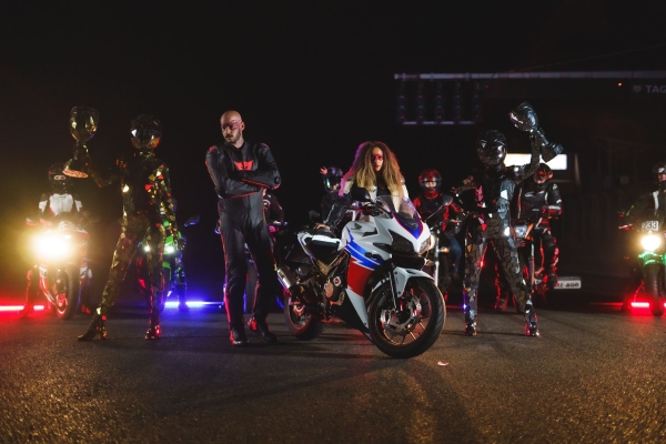 Skupina motorkárov vo farebnom oblečení sebavedomo stojí v noci. Jasné svetlomety ich osvetľujú a vytvárajú dynamickú a dobrodružnú scenériu.