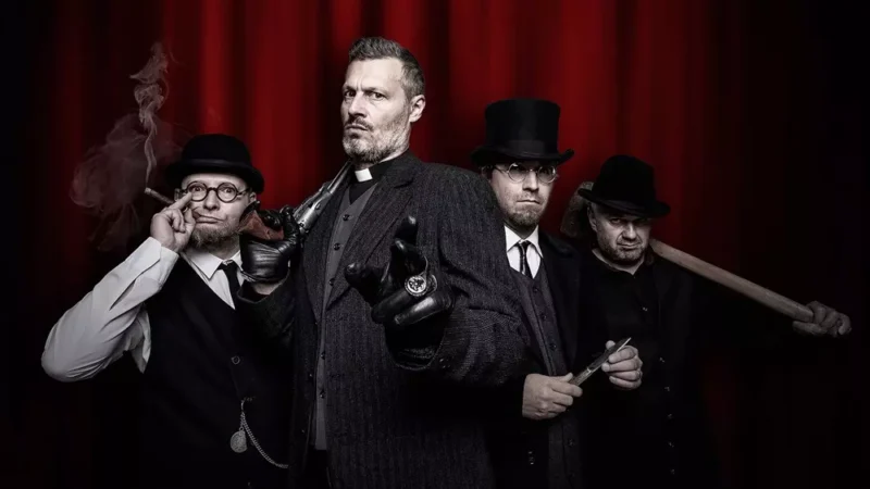 Štyria muži vo vintage oblečení stoja oproti červenej opone. Muž vpredu je v kňazskom odeve so zopnutými rukami, po stranách ho obklopujú muži v burinkách a kabátoch, jeden drží cigaru a druhý netopiera. Nálada je tajomná a napätá.