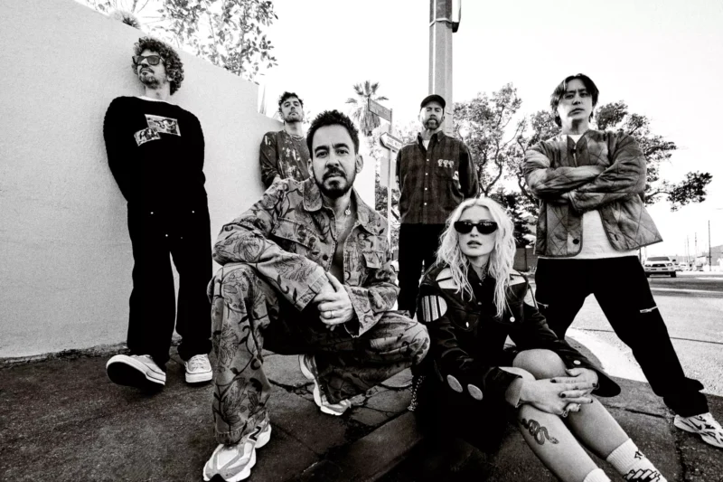 Šesť ľudí v mestskom oblečení sebavedomo pózuje na rohu ulice. Čiernobiela fotografia vyžaruje chladnú, drsnú atmosféru s uvoľneným, no zároveň asertívnym postojom.