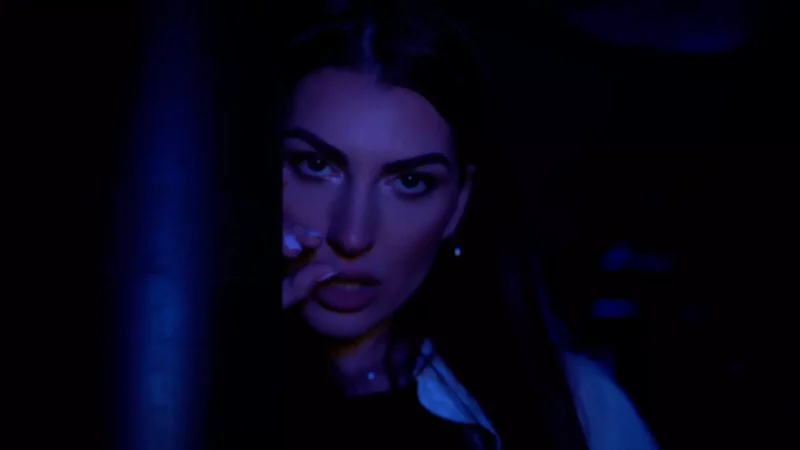 Žena s intenzívnymi očami čiastočne zakrytými tmavým stĺpom je zvýraznená melancholickým fialovým svetlom. Jej výraz vyjadruje tajomstvo a intrigu.