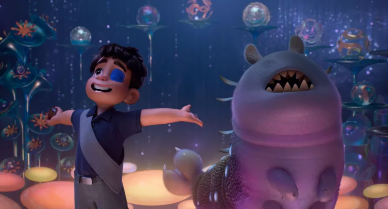 Usmievavé dieťa s náplasťou cez oko stojí s rozpaženými rukami vedľa priateľského stvorenia. Sú obklopené žiariacimi, farebnými guľami. Scéna je rozmarná a radostná.