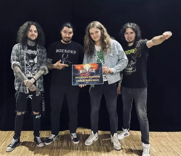 Štyria muži stoja spolu a držia nápis „Metal Battle National Winner Czech Republic“. Majú na sebe ležérne rockové oblečenie s čiernou oponou v pozadí.