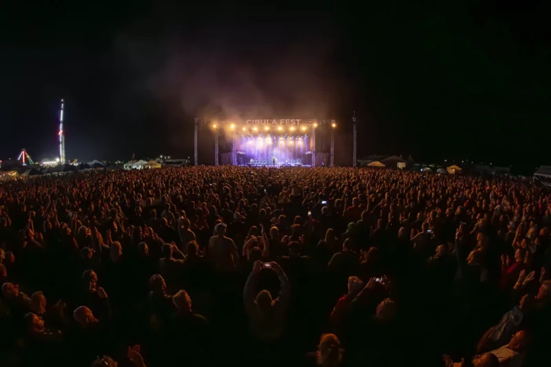 Dav na nočnom koncerte zhromaždenom pred jasne osvetleným pódiom s nápisom „Cibula Fest“. Nadšené publikum zachytáva živú atmosféru.Libor Ponca