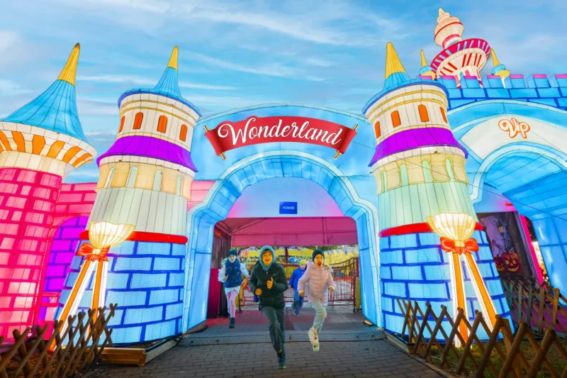 Deti vzrušene vybehli z jasného, farebného vchodu s označením „Krajina zázrakov“, ktorý je ozdobený hravými vežami a žiarivými svetlami na pozadí jasnej oblohy.