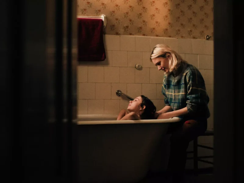 Žena s láskou umýva dieťa vo vintage vani. Obkladaná stena a kvetinová tapeta vytvárajú hrejivú, nostalgickú atmosféru. Scéna pôsobí nežne a intímne.