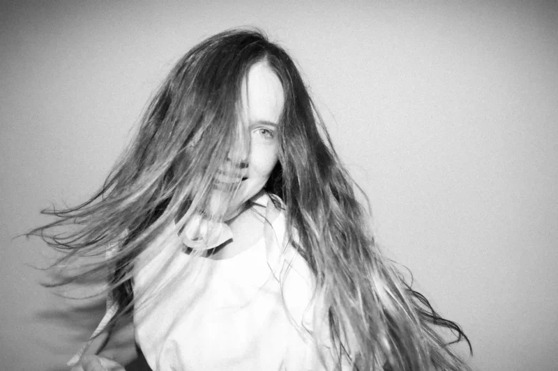 Čiernobiela fotografia radostne sa usmievajúcej osoby s dlhými vlasmi splývavými okolo tváre. Obrázok vyvoláva pocit pohybu a šťastia.