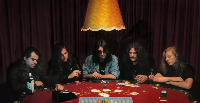 Päť dlhovlasých ľudí sa zhromaždilo okolo pokrového stola pod teplou lampou a skúmali karty a pokrové žetóny. Nálada bola napätá a sústredená.