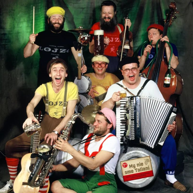 Veselá kapela siedmich hudobníkov pózuje s rôznymi nástrojmi, ako je gitara, saxofón, akordeón a bicie. Majú na sebe farebné, hravé oblečenie, ktoré vytvára živú a veselú atmosféru.