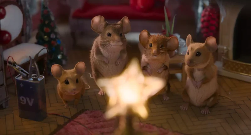 Štyri myši sa zhromaždili okolo žiariacej hviezdy v útulnej, slávnostnej miestnosti. Viditeľný je malý ozdobený vianočný stromček a 9V batéria. Teplá, radostná atmosféra.