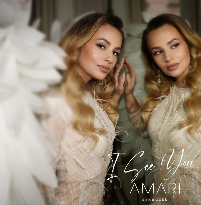 Blondínka v bielych šatách s detailmi sa s jemným úsmevom pozerá do zrkadla. Nápis znie „Vidím ťa, AMARI od roku 1988.“ Elegantný a zamyslený tón.