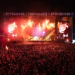 Veľký dav si užíva živý nočný koncert na festivale Pohoda 2025. Jasne osvetlené pódium žiari červenými a oranžovými svetlami, čo vytvára energickú atmosféru.