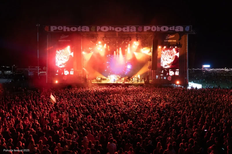 Veľký dav si užíva živý nočný koncert na festivale Pohoda 2025. Jasne osvetlené pódium žiari červenými a oranžovými svetlami, čo vytvára energickú atmosféru.
