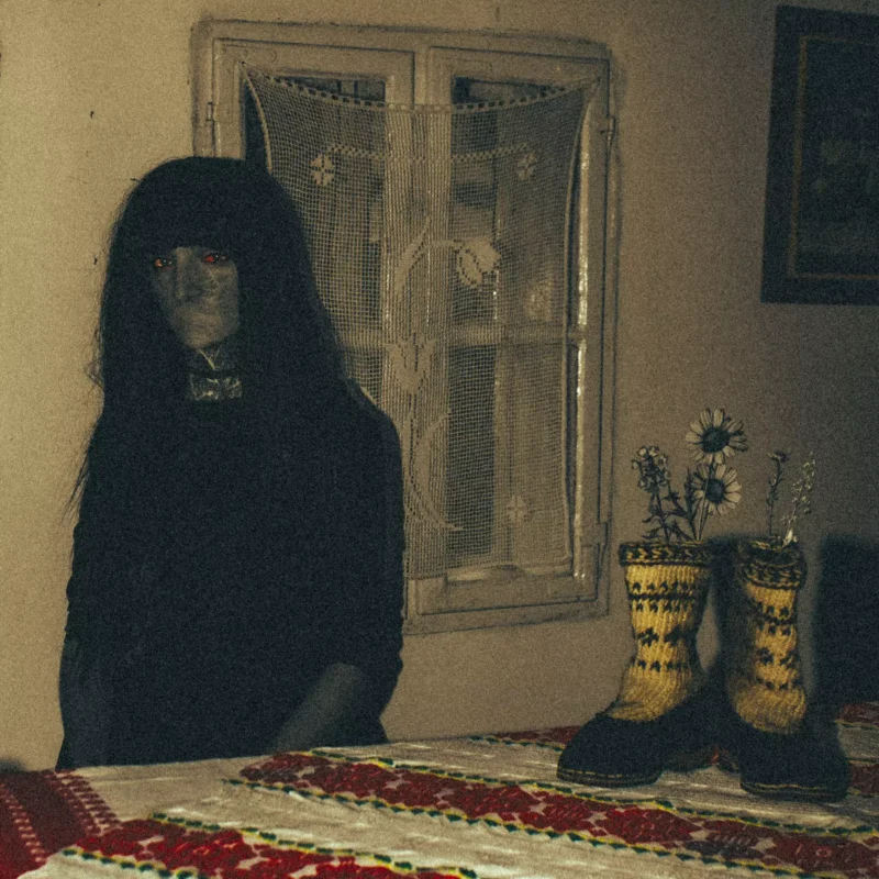 Pri okne sedí slabo osvetlená miestnosť so záhadnou postavou so žiariacimi červenými očami. Na stole s vyšívaným obrusom ležia pletené čižmy s kvetmi, ktoré vytvárajú strašidelnú atmosféru.