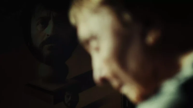 Detailný záber osoby sa vpravo javí ako rozmazaný, zatiaľ čo vľavo je viditeľný jasnejší odraz inej osoby. Obrázok pôsobí tajomne a introspektívne.