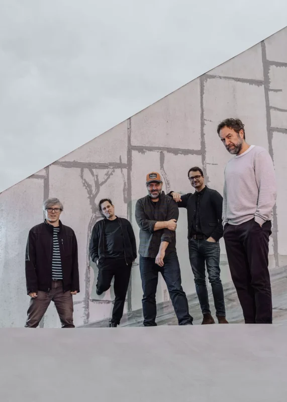 Päť mužov ležérne pózuje na pozadí moderného betónového pozadia. Ich výrazy vyžarujú uvoľnenú atmosféru, vyjadrujú kamarátstvo a zmysel pre ležérny štýl.