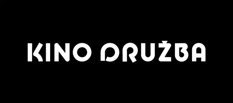 Tučný biely text „KINO DRUŽBA“ je vycentrovaný na jednoliatom čiernom pozadí. Moderné geometrické písmo vytvára elegantný a minimalistický vzhľad.