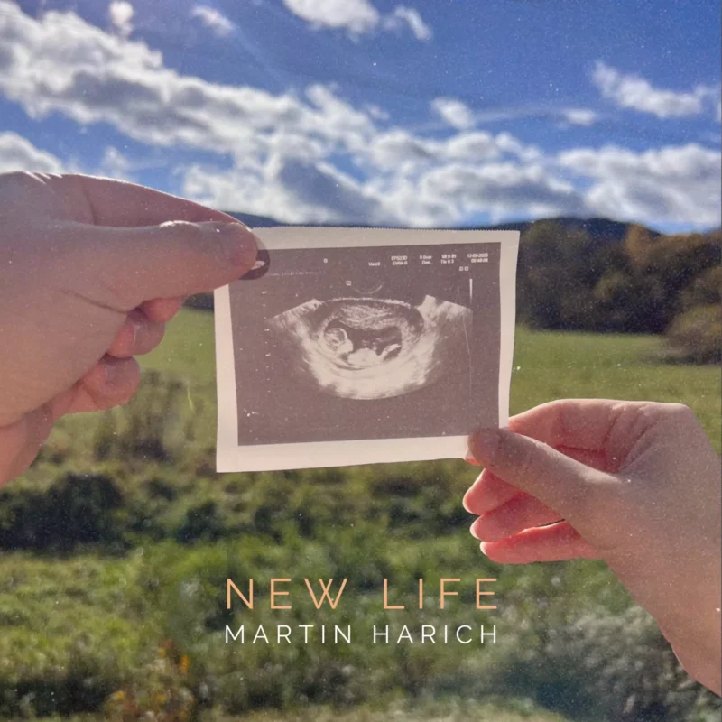 Ruky držiace čiernobielu ultrazvukovú fotografiu na pozadí jasnej, slnečnej krajiny so sviežou zeleňou a modrou oblohou. Text znie: „Nový život, Martin Harich.“