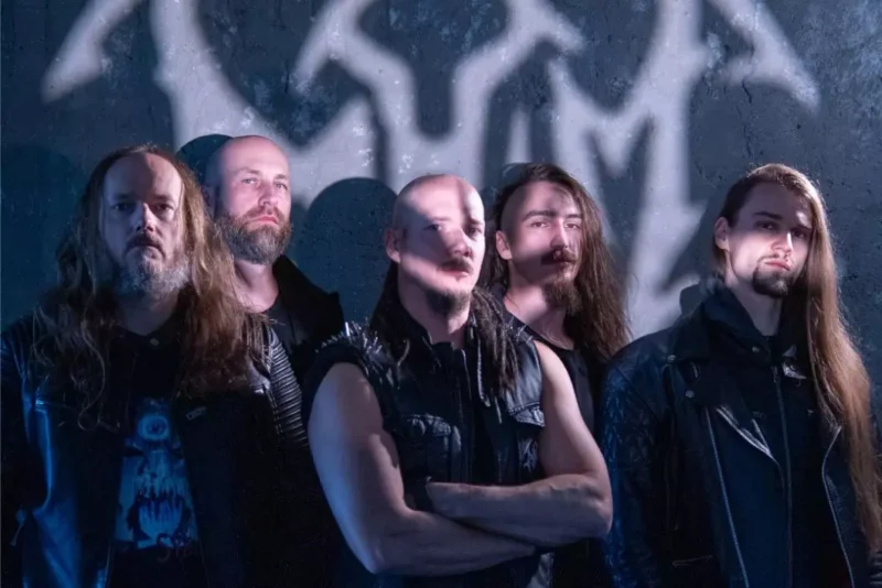 Päť mužov s dlhými vlasmi a bradami pózuje pred stenou s graffiti. Majú na sebe čiernu kožu a džínsy, z ktorých vyžaruje temný, vážny tón.