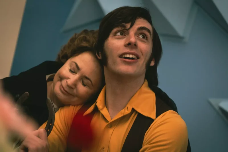 Muž v žltej košeli a veste s úsmevom zdvihne zrak. Žena si spokojne opiera hlavu o jeho rameno. Vládne vrúcna a láskavá atmosféra.