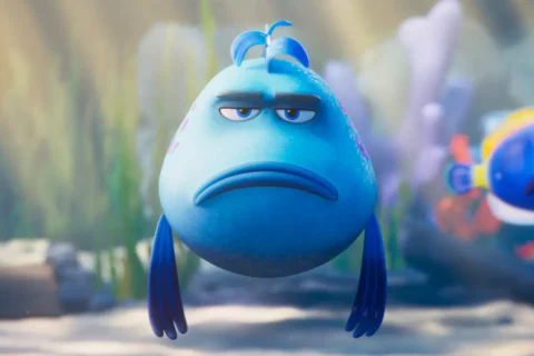 V podvodnej scéne pláva mrzutá modrá kreslená rybka s ovisnutými plutvami, zatiaľ čo iná farebná rybka sa pozerá z pozadia a vyjadruje humor.