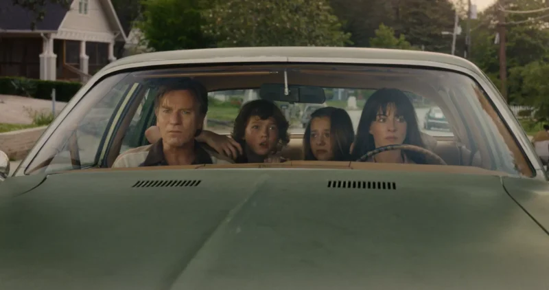 Štvorčlenná rodina napäto sedí v starom zelenom aute zaparkovanom na predmestskej ulici. Otec vyzerá odhodlane, zatiaľ čo matka s dvoma deťmi pôsobia úzkostlivo.