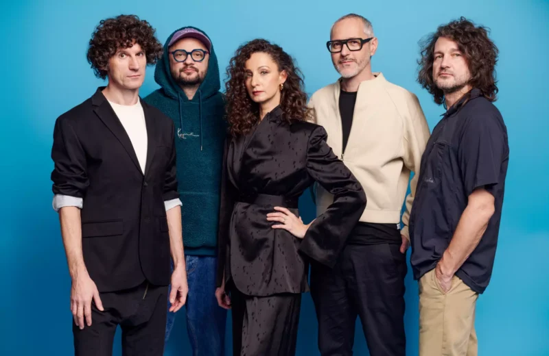 Skupina piatich ľudí stojí sebavedomo na modrom pozadí. Majú na sebe rôzne oblečenie, od ležérnych až po formálne, pričom všetky vyžarujú kreatívnu a štýlovú atmosféru.