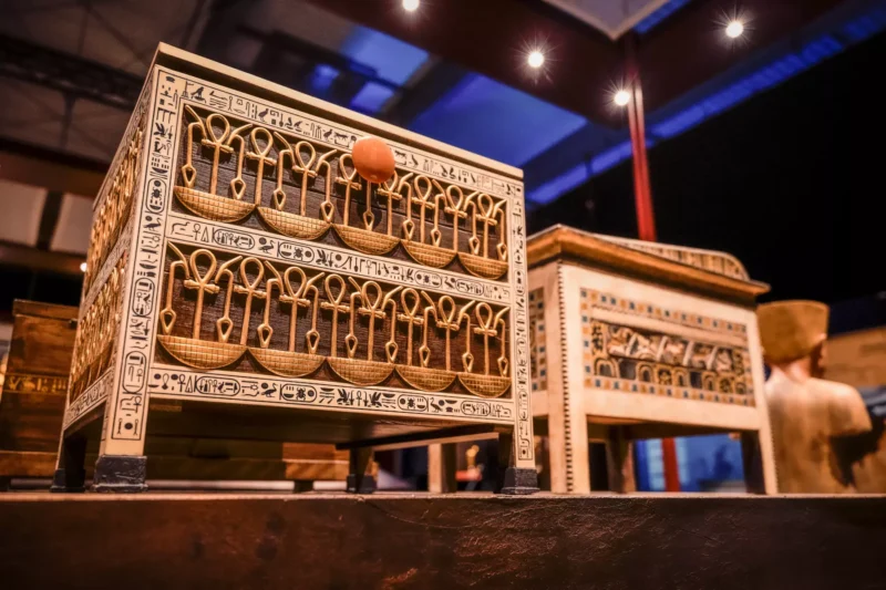 Zdobená egyptská truhlica so zlatými symbolmi Ankh a hieroglyfmi sa leskne v teplom svetle a evokuje pocit starodávneho remeselného spracovania a tajomstva.