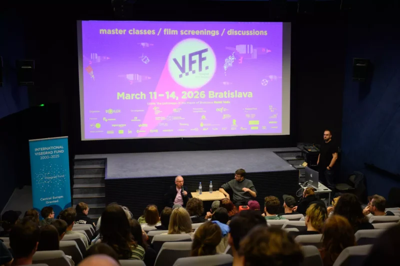 Publikum v divadle stojí oproti javisku s dvoma rečníkmi. Na veľkej obrazovke sa zobrazuje nápis „VFF“ a podrobnosti o podujatí, ktoré sa bude konať 11. – 14. marca 2026 v Bratislave. Atmosféra je angažovaná a profesionálna.