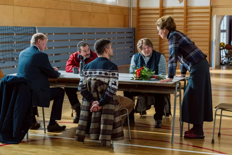 V telocvični sa okolo stola zhromaždilo päť ľudí. Jedna žena stála a rozprávala sa so štyrmi sediacimi mužmi. Všade vládla sústredená a vážna nálada.