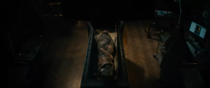 V slabo osvetlenej miestnosti leží na pitevnom stole múmia zabalená v otrhanej látke. Prostredie je strašidelné, s tieňovými rohmi a neďalekým počítačovým stolom.