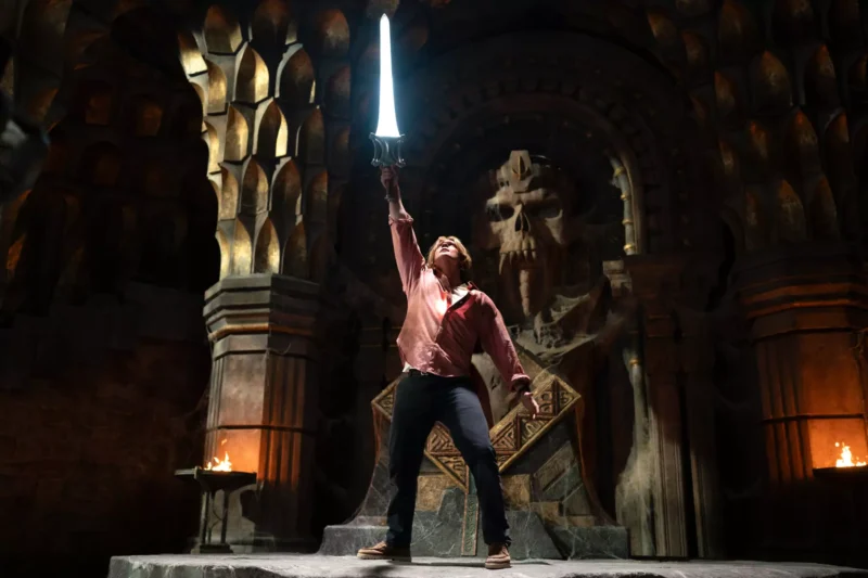 V tmavej, dramatickej komore so zdobenými stenami stojí víťazoslávne človek, držiac žiariaci meč vo vzduchu blízko veľkej vytesanej lebky, vyžarujúcej silu a odhodlanie.