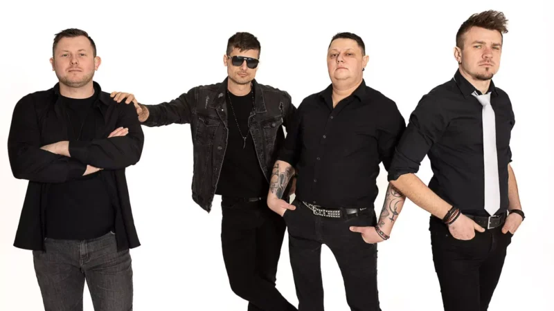 Štyria muži stoja sebavedomo na bielom pozadí, oblečení v čiernom oblečení. Jeden má slnečné okuliare, druhý má bielu kravatu. Všetci vyžarujú atmosféru rockovej kapely.