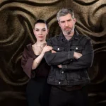Sebavedomý muž a žena stoja na abstraktnom, textúrovanom pozadí. Muž si prekríži ruky, čím vyjadruje silu, zatiaľ čo žena ho jemne drží za ruku.
