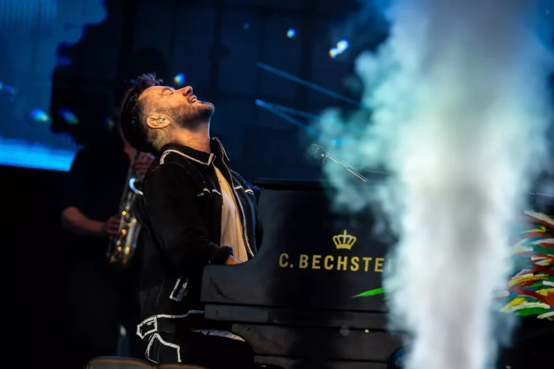 Hudobník vášnivo hrá na pódiu na klavíri C. Bechstein s hlavou zaklonenou v emóciách. Dym a farebné svetlá vytvárajú dramatickú atmosféru.