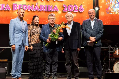 Päť ľudí pózuje na festivalovom pódiu; muž drží kvety, zatiaľ čo za nimi oslavne svieti farebný transparent „Berdárika 2026“.