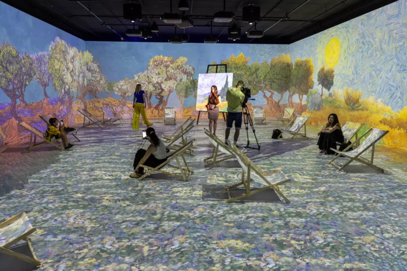 Pôsobivá umelecká inštalácia s krajinkami v štýle Van Gogha premietanými na steny a podlahu. Ľudia sedia na ležadlách a vytvárajú pokojnú atmosféru.