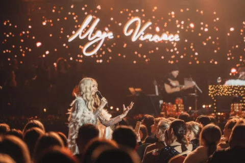 Blonďavá speváčka vystupuje pred sústredeným publikom pod žiariacim nápisom „My Universe“ a v teplom svetle pripomínajúcom hviezdy, čo vytvára intímnu a slávnostnú koncertnú atmosféru.